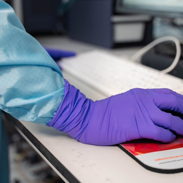 A scientists hand in rubber gloves using a mouse and keyboard